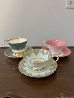 Three English porcelain teacups and saucers in blue, light blue, and pink with gold accents.