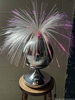 Front and side views of the vintage fiber optic lamp showing pink and violet light strands from rotating fan fibers above the polished chrome base on wooden stool.