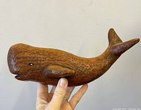 Hand holding carved wooden whale sculpture in side profile showing nail eye and textured wood carving details.