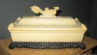 Front angled view of cream-colored molded Bakelite jewelry box with black decorative base and phoenix dragon lid handle.