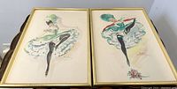 Pair of watercolor paintings by Alice Huertas showing Moulin Rouge can-can dancers in gold frames against a white floor background.