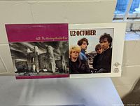 Two U2 vinyl album covers: 'The Unforgettable Fire' with castle image and magenta border, 'October' with band portrait on white background.