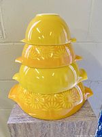 Stacked view of the set of 4 Pyrex vintage mixing bowls in orange daisy pattern and solid yellow-orange colors.