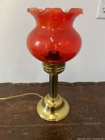 Front view of the table lamp showing the brass base and cranberry glass shade with ruffled top.