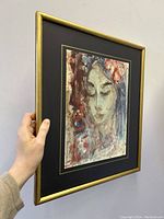 Framed watercolor portrait of a woman in a gold frame held by hand, showing size and framing.