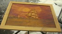 Frontal image of carved wood maritime scene with ship, lighthouse, and sunset in natural pine wood frame, outdoors in snow.