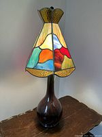 Front view of the table lamp on a wooden surface with the stained glass shade lit showing colors and design.