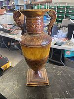 Front view of a 16 inch metal vase showing embossed decorative details, sculpted handles, and a wood-toned midsection.
