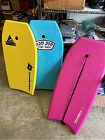 Photo showing three boogie boards standing up side by side. Yellow Beachwave Performance, blue Ron Jon Surf Shop, and pink Triangle 115.