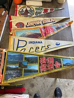 Five triangular vintage pennants laid out flat on the floor; includes sports and travel themes