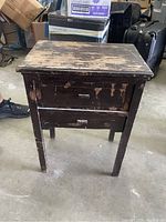 Front view of antique spool cabinet showing worn top surface, drawer, and four legs.