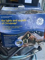 Box packaging showing festive house with Christmas light and music theme, indication of product features and usage for indoor/outdoor use.