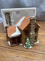 Front angled view of Timber Knoll miniature log cabin with snow on roof and stone chimney, power cord and box insert behind.