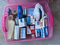Overview shot of a pink plastic tote containing first aid supplies including gauze pads, bandages, adhesive tapes, and zip ties.