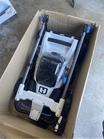 Folded Hart electric lawn mower inside a cardboard box, showing the handle and body.