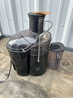 Front image of the black Jack LaLanne Fusion Juicer showing the clear pulp and juice containers and locking arm.