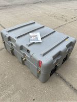 Large grey Pelican travel case photographed outdoors on pavement, showing top and side angles with manual on top.