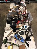 Overall view of the miscellaneous lot on a table showing various tools, collectibles, sporting goods items including green jack stands, flashlight, pouches, and assorted boxes