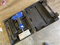 Blue Porter-Cable pneumatic nailer inside black carrying case with box of nails.