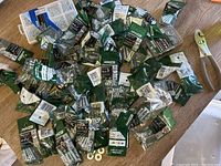 Overview of assorted new hardware items including nuts, bolts, washers, and machine screws in their original plastic bags on a wooden surface.