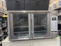 Front view of Oster large toaster oven showing stainless steel body, dual glass doors with handles, and digital control panel.