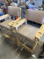 Two wooden billiards chairs side by side showing overall condition and design with upholstered seat and back, light wood finish, and built-in cup holders.