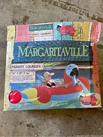 Original box of Margaritaville Parrot Lounger inflatable pool raft showing colorful parrot design and measurements: 86 x 52 x 36 inches.