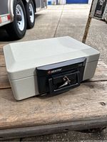 Closed view of light gray Sentry lock box safe model 1100 with key in lock, showing front handle and logo.