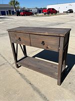 Three-quarter angled view of gray wash wooden sideboard table showing two drawers and lower shelf outdoors.