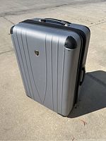 Front view of a large silver hard shell suitcase with black protective corners and a black zipper.
