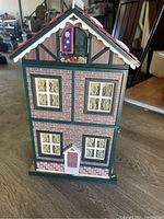 Front view of the closed tall Christmas music box shaped as a house with window details and a door.