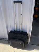 Black Targus rolling laptop suitcase upright with telescoping handle extended, visible exterior compartments, photographed outside against a white wall.