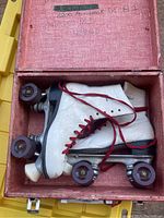 Overhead photo of the pair of white leather roller skates with red laces, red wheels, in pink textured carrying case showing interior lid with handwritten markings.