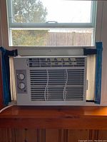 Front view of white GE window air conditioner installed in a window, showing rotary dial controls and installation panels.