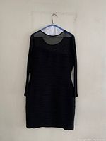 Front view of black cocktail dress on hanger, showing sheer neckline and long sleeves with textured horizontal wave pattern fabric body.