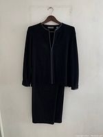 Full view of black wool pantsuit hanging on a wooden hanger, showing jacket and pants.