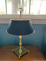 Full view of the blue table lamp with brass base sitting on wooden surface in front of window.