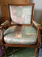 Front view of the wooden armchair showing upholstered seat and back with pastel colored fabric and detailed carved wooden frame.