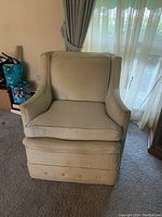 Front view of one light-colored upholstered club chair with cushioned seat and back, button-tufted skirt, showing wear and discoloration.