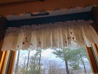 View of one set of light-colored curtains with gathered rod pocket and floral embroidery at the bottom