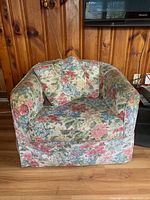 Photo of a floral upholstered armchair against a wood-paneled wall, showing overall shape and fabric pattern