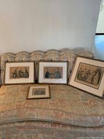 Four framed vintage style fashion prints displayed on a floral patterned sofa, showing detailed 19th-century costumes.
