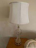 Photo of one glass table lamp with a clear ornate cut-glass base paired with a white fabric lampshade.