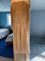 Full front view of gold beaded gown showing long sleeves, detailed beading on upper portion, and pleated skirt hanging naturally.