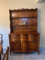 Full front view of a wooden hutch with two open shelves on the top and three lower drawers with two paneled doors beneath.
