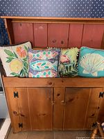 Four outdoor pillows lined up on a wooden bench, each pillow featuring a unique nature-themed design.