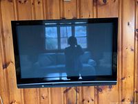 Front view of Panasonic TV mounted on wooden wall, showing screen and frame, some reflections visible.
