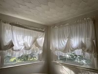 Two sets of white sheer curtains hanging on windows, showing ruffled bottom edges and eyelet headers.