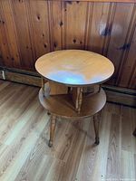 Front angle of the wooden two-tier round side table showing smooth top and lower shelf with turned legs and casters