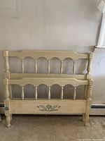 Twin headboard and footboard painted cream with turned spindles and green floral designs, showing signs of wear and fair condition.